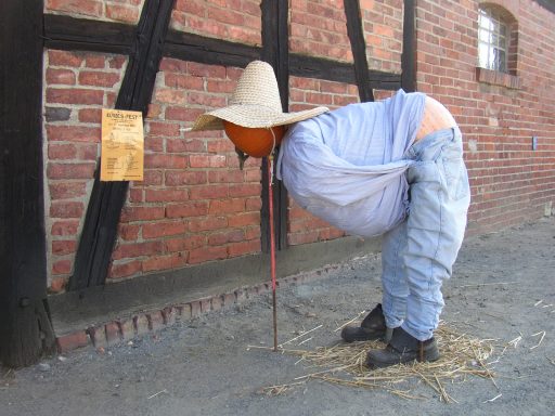 gebastelte Kürbisfigur mit Jeans, Jeanshemd und Hut, der Kopf ist ein Kürbis, der Po ist aus zwei rosafarbigen Kürbissen geformt und sichtba