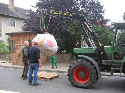 Trecker mit Frontlader, der einen Riesenkürbis in einem Big Bag hochhebt