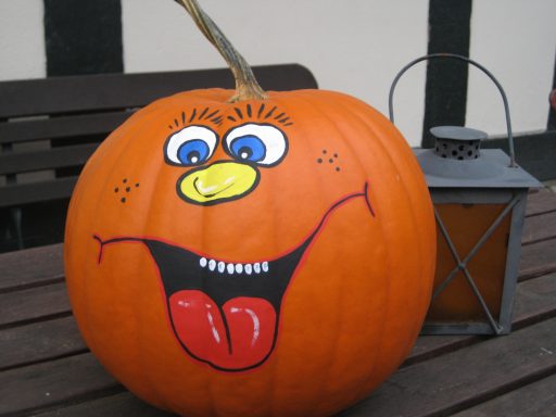 Ein orangener Halloweenkürbis, nicht geschnitzt, dafür mit einem Gesicht und großen offenen Mund mit Zunge bemalt